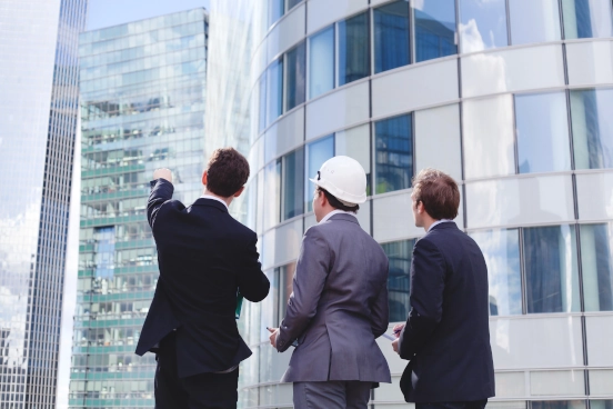 Une image de trois personnes devant un bâtiment pointant vers lui. L’une des personnes porte un casque de sécurité.