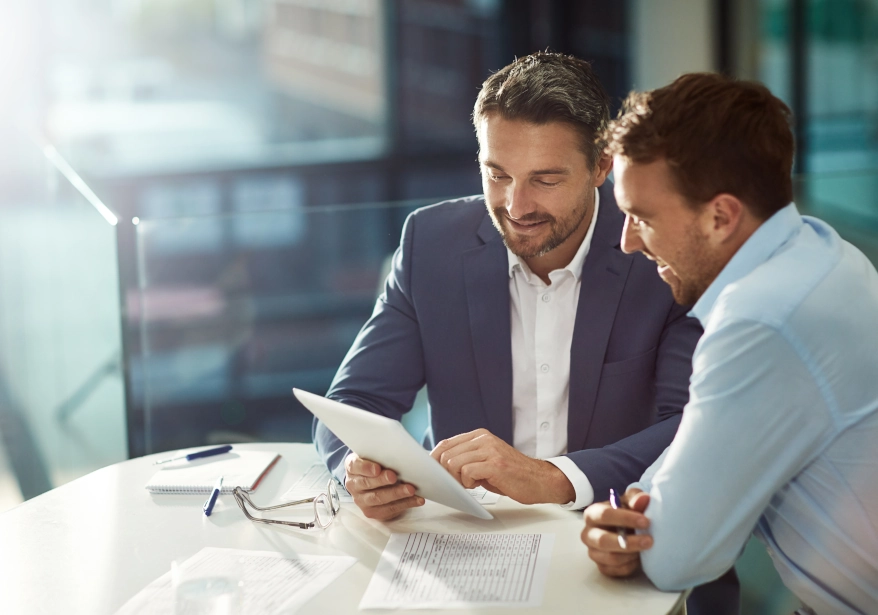 A photograph of two men sat together at a table looking at a document