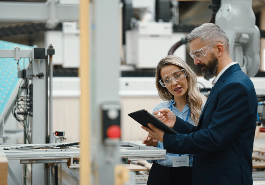 A photograph of two people in a manufacturing environment reviewing information on a tablet screen